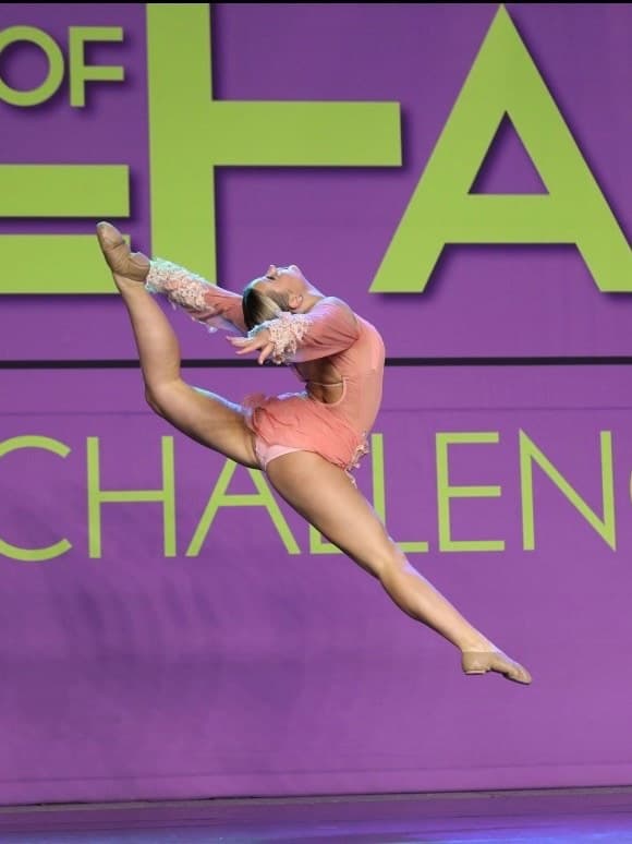 Avery Zenz mid-leap on stage at a dance competition